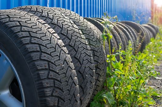 sets of car tires with disks are on the street on the ground near the fence of the cottage against the background of glare from the sun