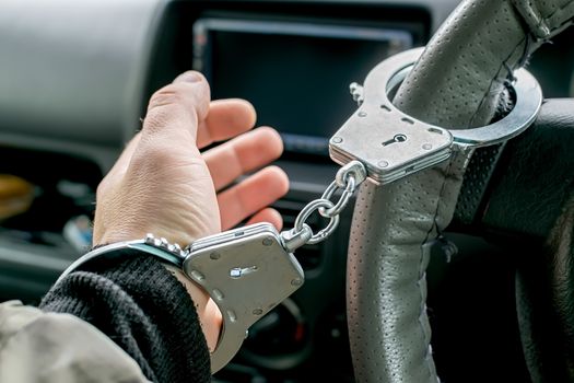 car driver's hand handcuffed to steering wheel, arrest, driving ban by traffic violator