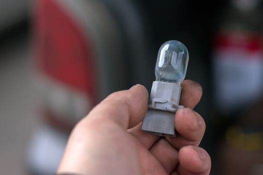 new and burnt out car light bulb, in man's hand