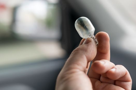 the fingers of the human hand hold the damaged light bulb in the car