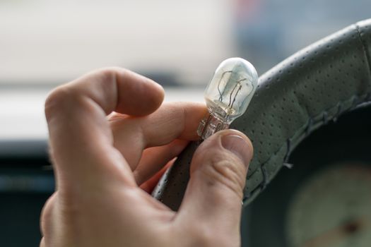 the fingers of the human hand hold the damaged light bulb in the car