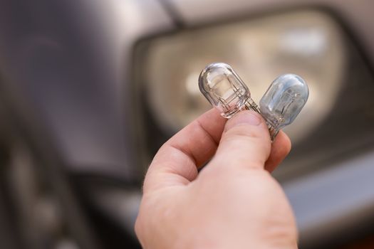 new and burnt out car light bulb, in man's hand