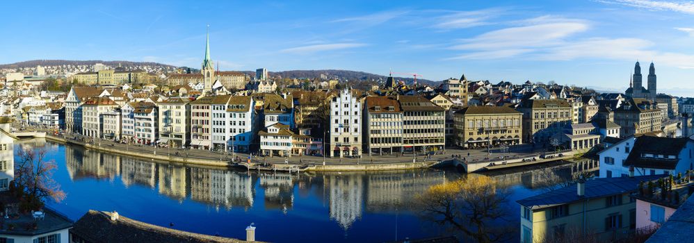 ZURICH, SWITZERLAND - DECEMBER 27, 2015: Panoramic view of the east bank of the Limmat River, with the Predigerkirche and Grossmunster churches, locals and visitors. In Zurich, Switzerland
