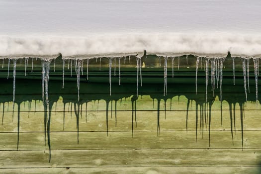 icicles on the eaves of the roof of a wooden house are melting in the sun