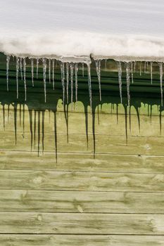 icicles on the eaves of the roof of a wooden house are melting in the sun