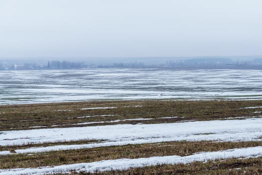 field with melting snow and last year's grass at the end of winter