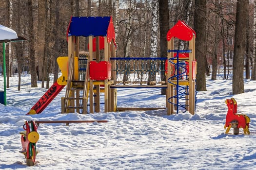 playground in the park in winter under snow on a sunny day