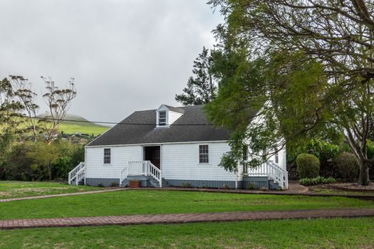 Waimea, Hawaii, USA. - January 15, 2020: Parker Ranch headquarters. White wooden house surrounded by green trees behind green lawn and under light blue cloudscape.