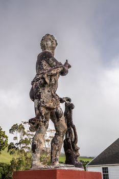 Waimea, Hawaii, USA. - January 15, 2020: Parker Ranch headquarters. Closeup of old white stone discollored by black mold statue of Apollo under light blue sky. Some green foliage.
