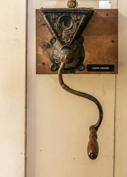 Waimea, Hawaii, USA. - January 15, 2020: Parker Ranch headquarters. Old brown metal-wood coffee grinder with long handle fixed to beige painted wall.