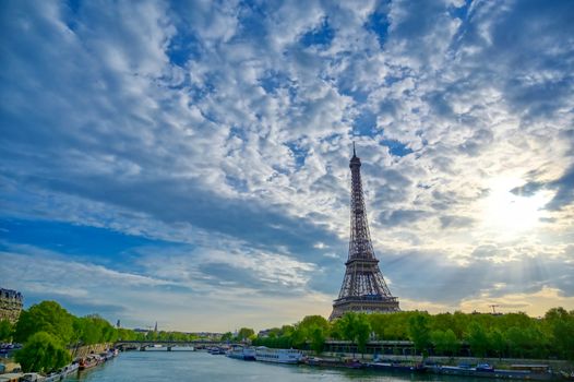The Eiffel Tower across the Seine River in Paris, France on a sunny day with beautiful clouds.