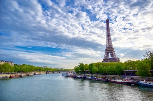 The Eiffel Tower across the Seine River in Paris, France on a sunny day with beautiful clouds.