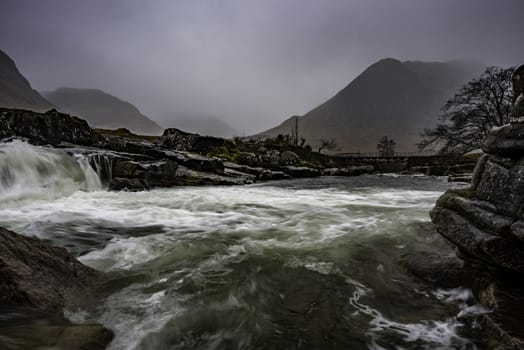 Glencoe, Scotland - Jan 2020: Water running over mountain wiers under the peaks at Glencoe in the Highlands of Scotland during winter 