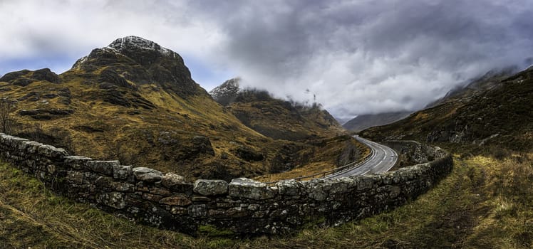 Glencoe, Scotland - Jan 2020: Panpramic view along a mountain road on the 3 sisters as a winter storm passes overhead