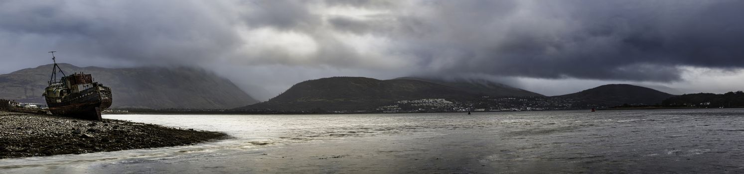Glencoe, Scotland - Jan 2020: Panorama of moody skies hanging over the boat wreck of the Corpach, with Ben Nevis and Fort William behind.
