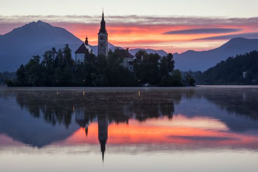 Dramatic sunrise on lake Bled, sunrise view on Bled lake, island, Pilgrimage Church of the Assumption of Maria and Castle with mountain range (Stol, Vrtaca, Begunjscica). Bled, Slovenia,