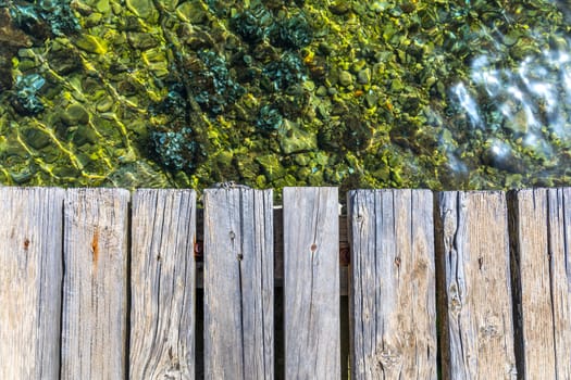 Wooden board empty over sea, can be used for display or present a product. Summer season. Empty perspective wooden planks over the reflection of green water, product display template.