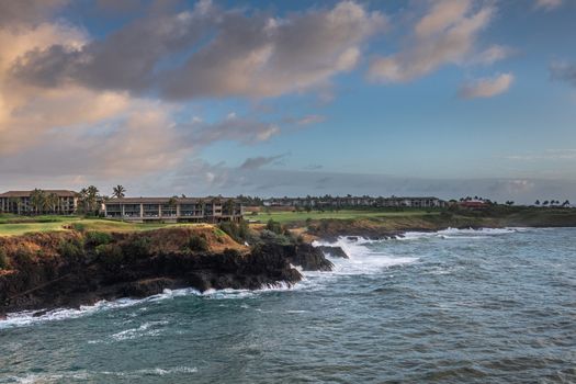 Nawiliwili, Kauai, Hawaii, USA. - January 16, 2020: Early morning light on Marriott resort behind green golf course under blue cloudscape. Blue ocean crashes white on black shoreline.