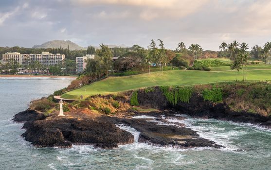 Nawiliwili, Kauai, Hawaii, USA. - January 16, 2020: Early morning light on Kukii Point lighthouse or beacon on black lava rock peninsula and golf couse with Kalapaki bay and beach and Marriott Beach Resort in back.