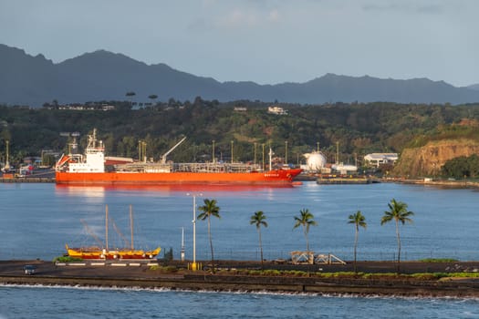 Nawiliwili, Kauai, Hawaii, USA. - January 16, 2020: Early morning light on red Marigola LPG tanker in port under light blue sky. Green belt on hill. Blue ocean water and pier in front with historic sail boat.