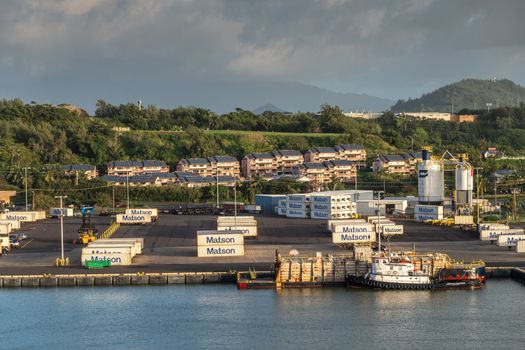 Nawiliwili, Kauai, Hawaii, USA. - January 16, 2020: Early morning light on dock in the port with Matson container yard. Green tree belt and houses in back under brown and light blue sky. Tugboat and barge.