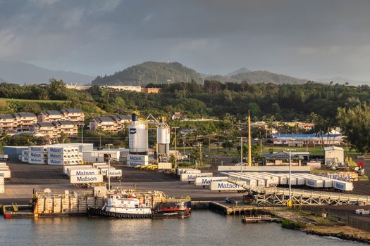 Nawiliwili, Kauai, Hawaii, USA. - January 16, 2020: Early morning light on dock in the port with Matson container yard. Green tree belt in back under brown and light blue sky. Tugboat and barge in front.