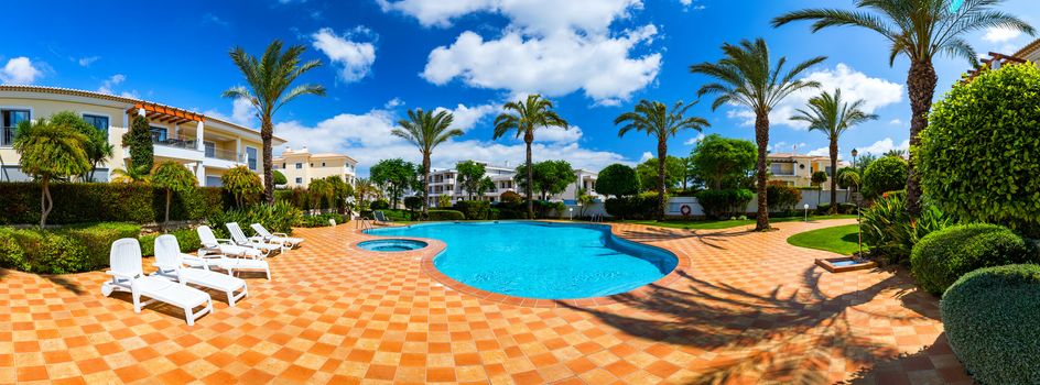 Great backyard with swimming pool, hot tub and lounge chairs. Swimming pool in backyard. Incredible swimming pool and garden with palm trees and flowers in a sunny day.