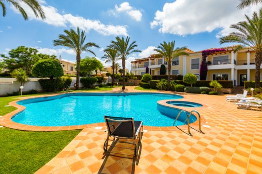 Swimming pool, sun-loungers and palm trees during a warm sunny day, paradise destination for vacations. Backyard swimming pool with garden full of palm trees and flowers. Backyard with swimming pool.