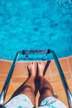 Relaxing at the swimming pool. Man relaxing next to swimming pool. Man enjoying the hot summer at swimming-pool. Sunbathing by the swimming pool, mans legs lying down on a sun lounger over the water.