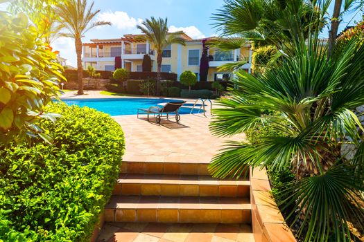 Great backyard with swimming pool, hot tub and lounge chairs. Swimming pool in backyard. Incredible swimming pool and garden with palm trees and flowers in a sunny day.