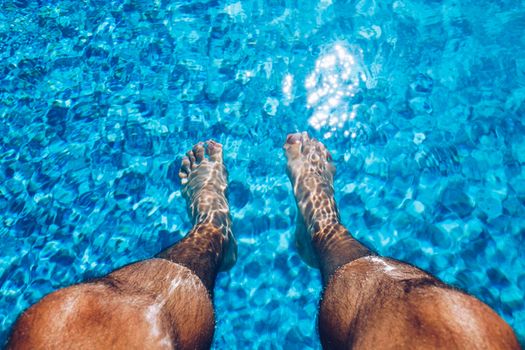 Relaxing at the swimming pool. Man relaxing next to swimming pool. Man enjoying the hot summer at swimming-pool. Sunbathing by the swimming pool, mans legs lying down on a sun lounger over the water.