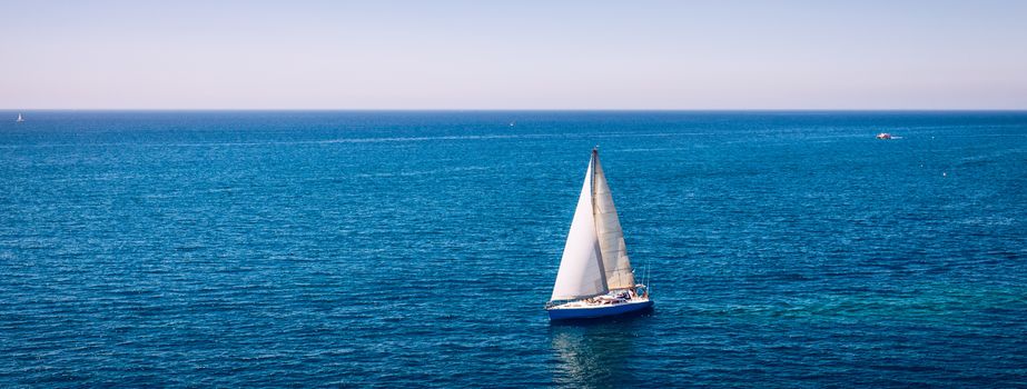 White sail boat isolated in blue sea water. Sailboat in the sea in the sunlight, luxury summer adventure, active vacation in Mediterranean sea. Yacht sailing on opened sea. Sailing boat. 