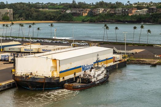 Nawiliwili, Kauai, Hawaii, USA. - January 17, 2020: Floating barge in port with white warehouse on top to cover shipping containers carries the Matson brand. Greenish ocean water. Green belt with housing.