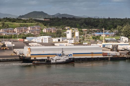 Nawiliwili, Kauai, Hawaii, USA. - January 17, 2020: Floating barge in port with white warehouse on top to cover shipping containers carries the Matson brand. Housing and green hills under blue cloudscape.