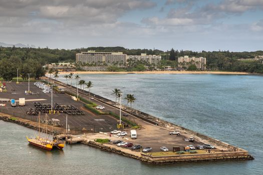 Nawiliwili, Kauai, Hawaii, USA. - January 17, 2020: South reef platfom of port built into sea water with Marriott Resort and beach in back, enveloped in green trees. Blue ocean water under gray cloudscape.