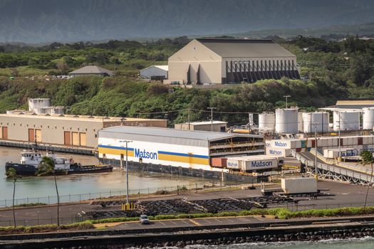 Nawiliwili, Kauai, Hawaii, USA. - January 17, 2020: Matson covered shipping container barge with puilling tugboat. Guardian Self Storage werehouse on green hill. All under dark rainy sky.