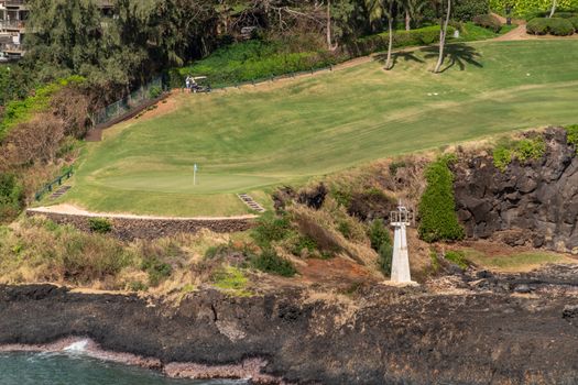 Nawiliwili, Kauai, Hawaii, USA. - January 17, 2020: Timbers Kauai Ocean green Golf Course with Kukii lighthouse or beacon on black lava rock up front.