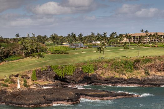 Nawiliwili, Kauai, Hawaii, USA. - January 17, 2020: Wide view over Timbers Kauai Ocean green Golf Course with Kukii lighthouse or beacon on black lava rock up front. Cloudscape and greenish ocean water.