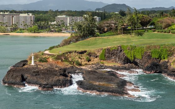 Nawiliwili, Kauai, Hawaii, USA. - January 17, 2020: Wide view over Marriott beach resort, green golf course with Kukii lighthouse or beacon on black lava rock up front. Greenish ocean water.