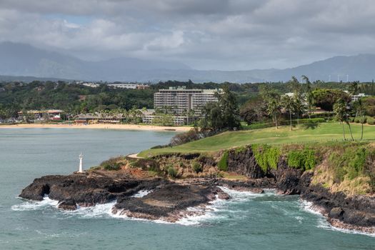 Nawiliwili, Kauai, Hawaii, USA. - January 17, 2020: Wide view over Marriott beach resort, green golf course with Kukii lighthouse or beacon on black lava rock up front. Greenish ocean water., Cloudscape.