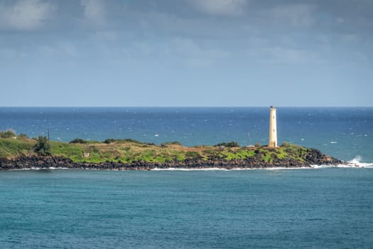 Nawiliwili, Kauai, Hawaii, USA. - January 17, 2020: Yellow Ninini lighthouse on black ocean-shore rocks of its green lands end. Blue ocean and sky..