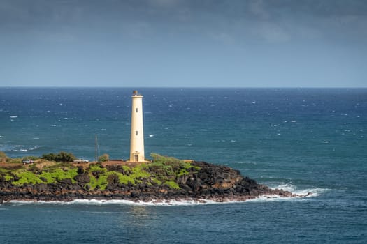 Nawiliwili, Kauai, Hawaii, USA. - January 17, 2020: Closeup of Yellow Ninini lighthouse on black ocean-shore rocks of its green lands end. Blue ocean and sky..