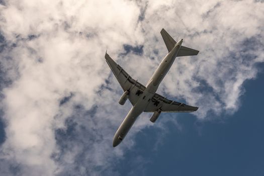 Nawiliwili, Kauai, Hawaii, USA. - January 17, 2020: Closeup of gray underbelly of flying airplane landing at airport captured against blue sky with white clouds. 