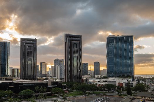 Honolulu  Oahu, Hawaii, USA. - January 18, 2020: Two identical iconic skyscrapers along South Street near waterfront plaza under  sunrise cloudscape. More buildings in back. Green vegetation in front.
