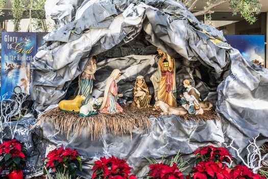Garden Grove, California, USA - December 13, 2018: Crystal Christ Cathedral. Statues in Nativity Scene for Christmas without baby Jesus but parents, animals and shepherds present. Red Poinsettia flowers up front.