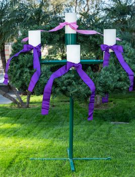Garden Grove, California, USA - December 13, 2018: Crystal Christ Cathedral. Closeup of the Advent Wreath in the garden. Green backgroound, four white candles, purple and pink ribbons.