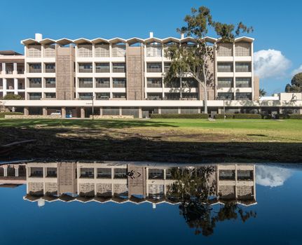 Santa Barbara, California, USA - January 6, 2019: The white and beige modern chemistry building of UCSB, behind green lawn and under blue sky. Also reflected in rain pool.