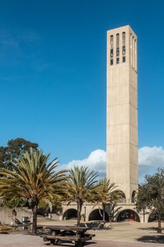 Santa Barbara, California, USA - January 6, 2019: The beige sleek and tall Bell Tower of UCSB,  under blue sky. Some tree vegetation around.