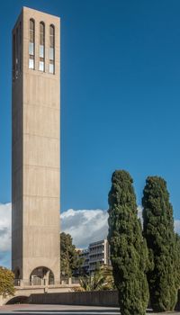 Santa Barbara, California, USA - January 6, 2019: The beige sleek and tall Bell Tower of UCSB,  under blue sky. Some tree vegetation around.