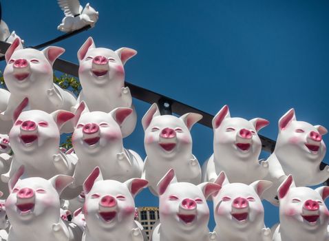 Sydney, Australia - February 9, 2019: Closeup of large display of 12 laughing pig dolls at First Fleet Park downtown to celebrate Chinese Year of the Pig. White skin with pink features, Blue sky.